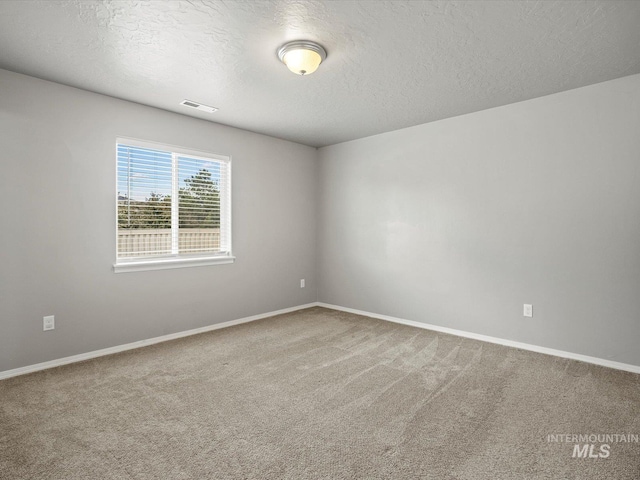 carpeted spare room featuring a textured ceiling and baseboards