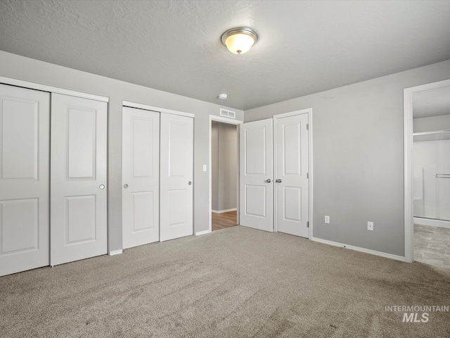 unfurnished bedroom with two closets, carpet floors, baseboards, and ensuite bathroom