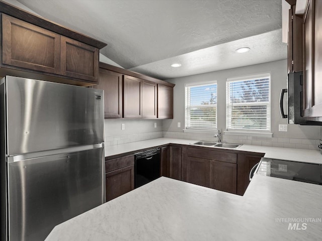 kitchen featuring appliances with stainless steel finishes, a sink, a textured ceiling, light countertops, and vaulted ceiling