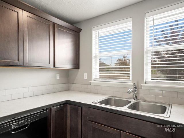 kitchen with black dishwasher, a sink, dark brown cabinets, healthy amount of natural light, and a textured ceiling
