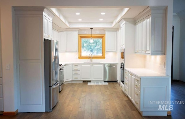 kitchen with sink, white cabinetry, decorative light fixtures, stainless steel appliances, and light hardwood / wood-style floors