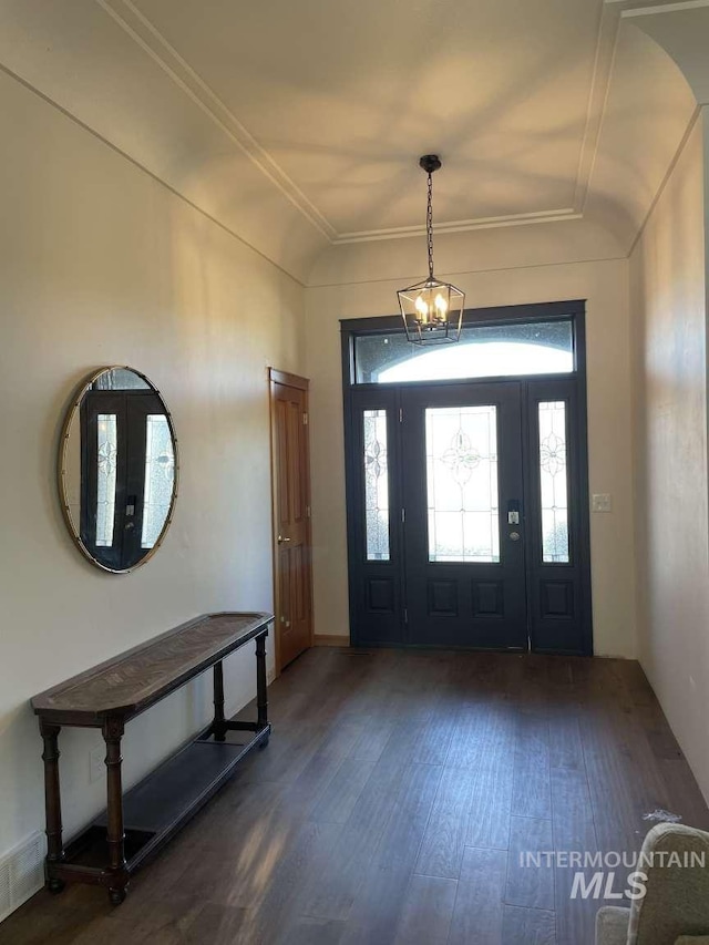 foyer entrance with vaulted ceiling, dark wood-type flooring, a notable chandelier, and ornamental molding