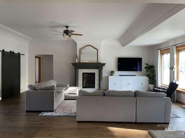 living room with beamed ceiling, dark hardwood / wood-style flooring, ceiling fan, crown molding, and a barn door