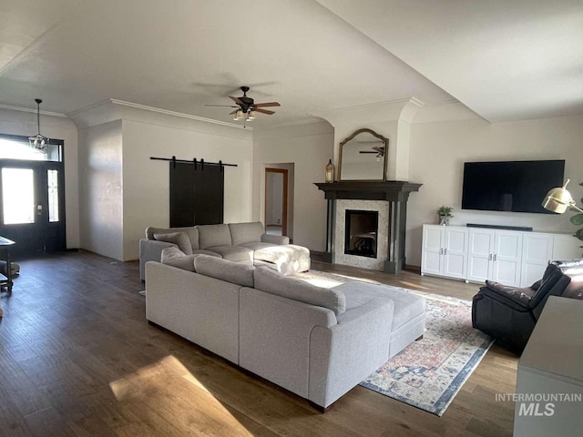 living room with dark hardwood / wood-style floors, ornamental molding, a barn door, and ceiling fan