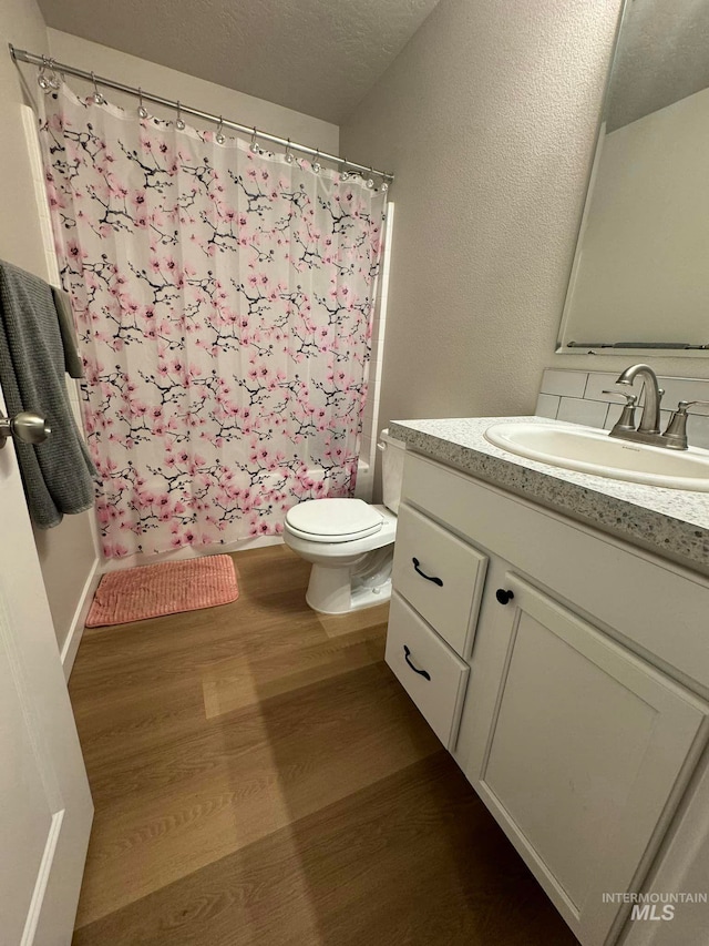 bathroom featuring curtained shower, toilet, vanity, wood finished floors, and a textured ceiling