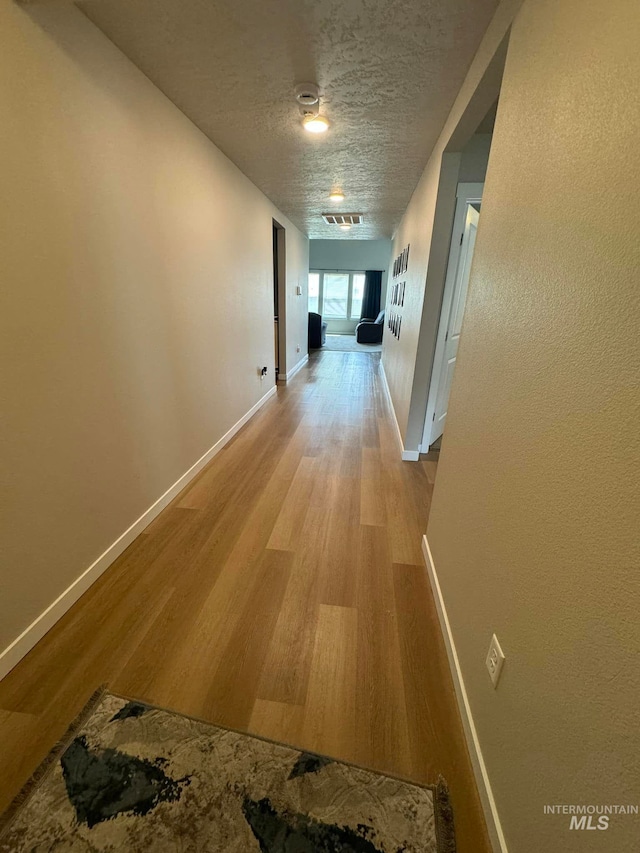 corridor with light wood finished floors, visible vents, a textured ceiling, and baseboards