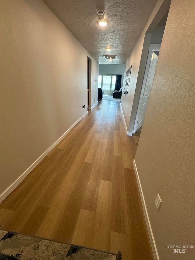 hall with baseboards, light wood-style floors, visible vents, and a textured ceiling