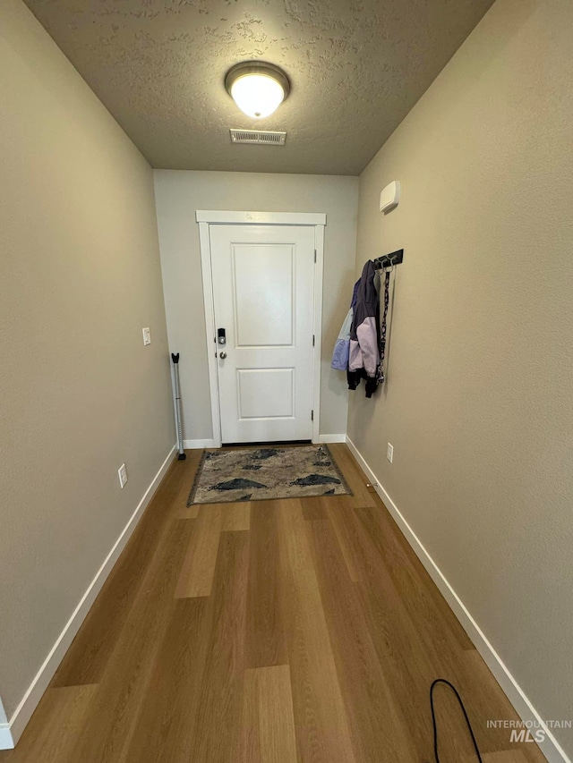 entryway featuring a textured ceiling, wood finished floors, visible vents, and baseboards