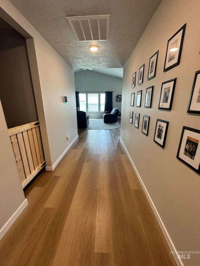 hall featuring visible vents, baseboards, a textured ceiling, and wood finished floors