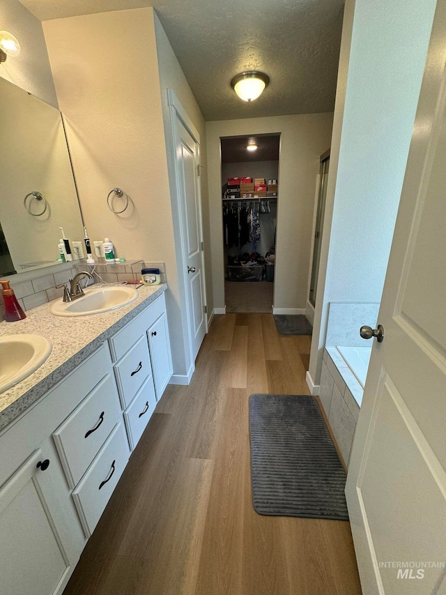 bathroom featuring a walk in closet, double vanity, wood finished floors, a textured ceiling, and a sink