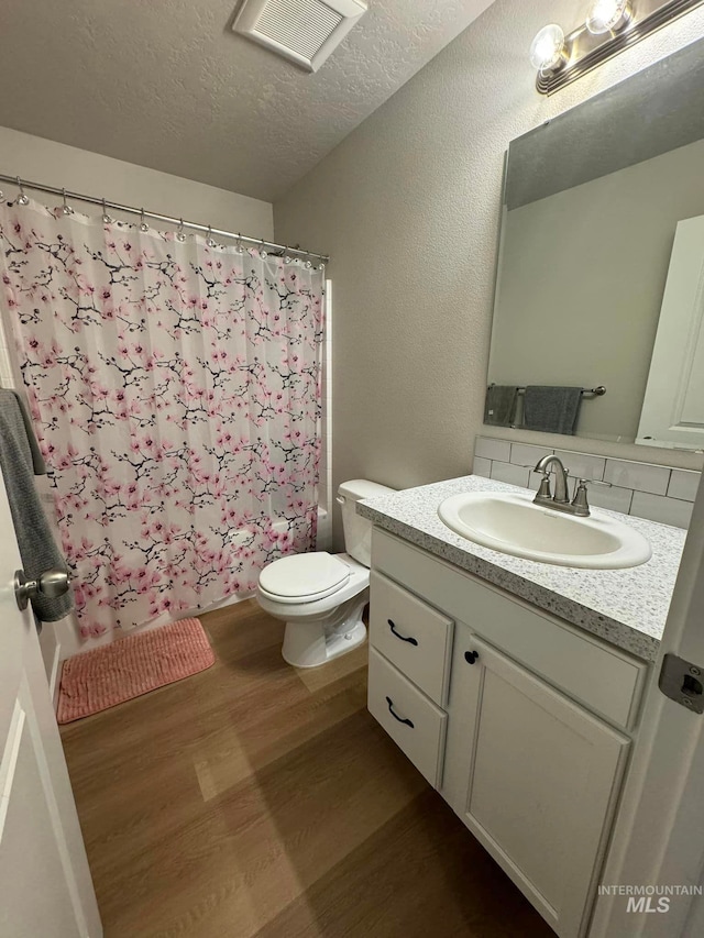 full bathroom featuring curtained shower, toilet, vanity, wood finished floors, and a textured ceiling