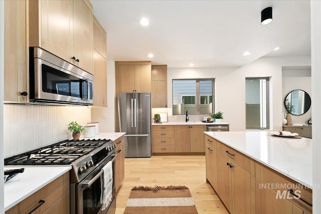 kitchen featuring appliances with stainless steel finishes, backsplash, sink, light brown cabinets, and light hardwood / wood-style flooring