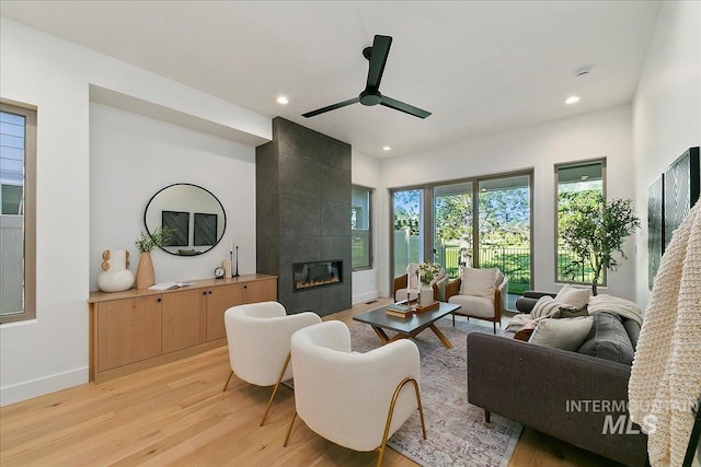 living room featuring a tile fireplace, ceiling fan, and light hardwood / wood-style flooring