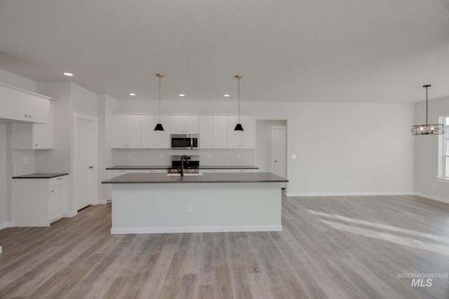kitchen with dark countertops, tasteful backsplash, a center island with sink, stainless steel microwave, and recessed lighting