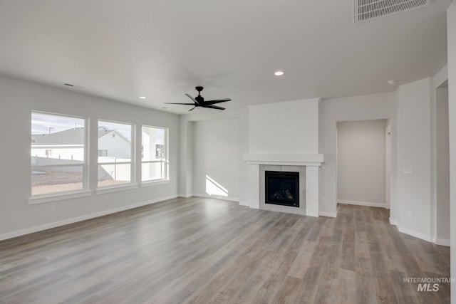 unfurnished living room featuring a tile fireplace, wood finished floors, visible vents, a ceiling fan, and baseboards
