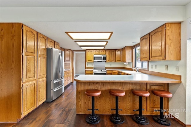 kitchen featuring stainless steel appliances, sink, a breakfast bar, kitchen peninsula, and dark wood-type flooring