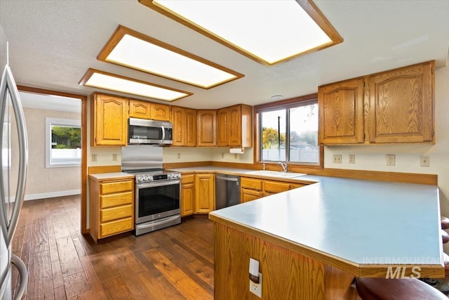 kitchen featuring stainless steel appliances, kitchen peninsula, a textured ceiling, sink, and dark hardwood / wood-style floors