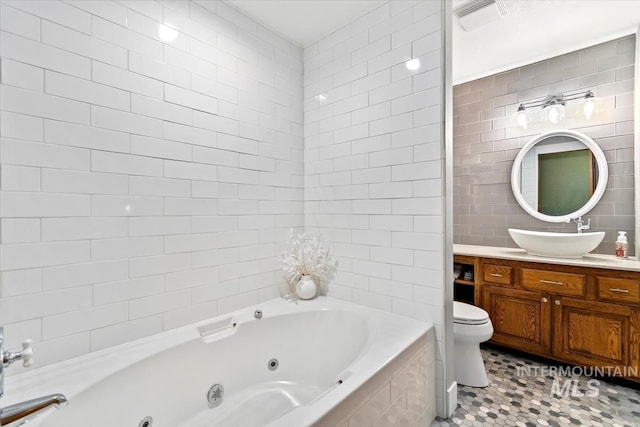 bathroom featuring tile patterned flooring, vanity, tiled bath, toilet, and tile walls