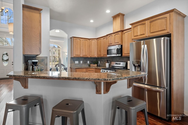 1814 E Grand Canyon Dr, Meridian, ID 83646 - kitchen with a breakfast bar area, backsplash, a peninsula, dark stone counters, and stainless steel appliances