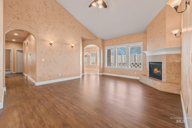 unfurnished living room featuring ceiling fan, dark hardwood / wood-style flooring, a tile fireplace, and high vaulted ceiling