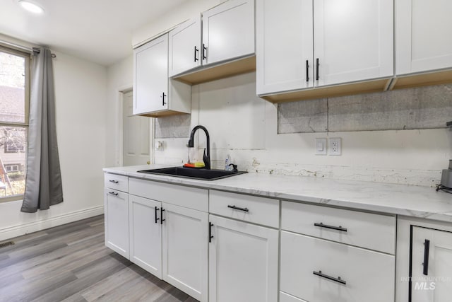 317 W C, Shoshone, ID 83352 - kitchen featuring light stone countertops, a sink, baseboards, white cabinets, and light wood-style floors