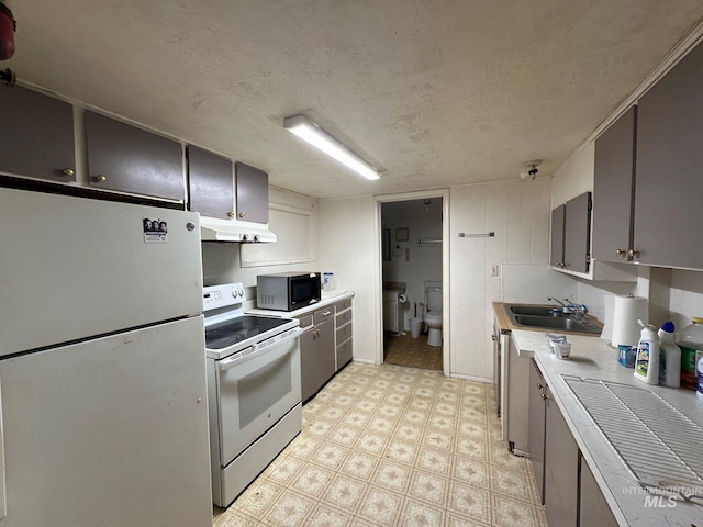 kitchen with under cabinet range hood, white appliances, a sink, light countertops, and light floors