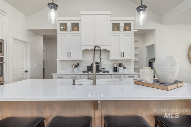 11304 W Helenium Dr, Star, ID 83669 - kitchen featuring lofted ceiling, decorative backsplash, light countertops, pendant lighting, and glass insert cabinets