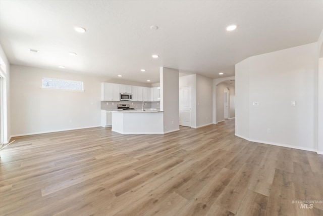 unfurnished living room with recessed lighting, arched walkways, light wood finished floors, and baseboards