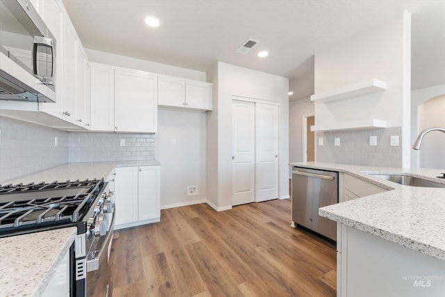 kitchen with open shelves, light stone counters, a sink, white cabinetry, and stainless steel appliances