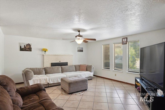 living room with a ceiling fan, a fireplace, baseboards, light tile patterned floors, and a textured ceiling