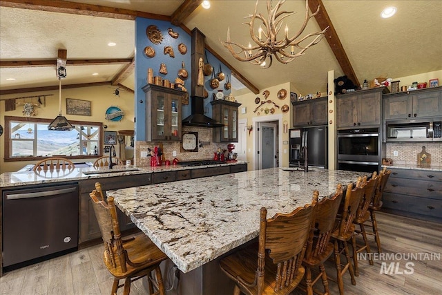 kitchen with sink, vaulted ceiling with beams, tasteful backsplash, a large island with sink, and black appliances