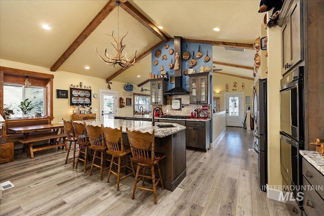 kitchen featuring tasteful backsplash, wood-type flooring, vaulted ceiling with beams, light stone counters, and a center island with sink