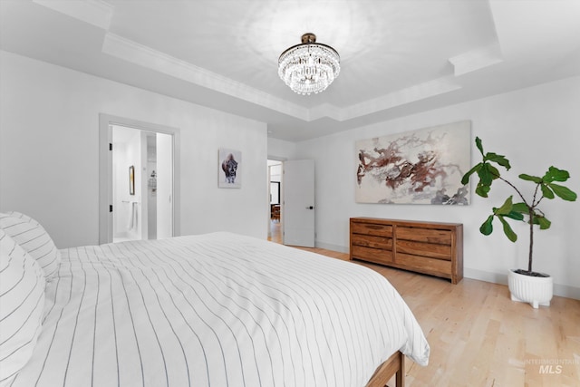 bedroom with a raised ceiling, an inviting chandelier, and light wood-type flooring