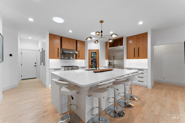 kitchen with decorative light fixtures, a kitchen bar, a center island, stainless steel built in fridge, and wall chimney range hood