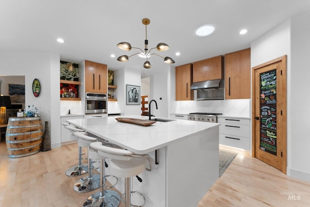 kitchen with sink, oven, white cabinets, a center island with sink, and exhaust hood