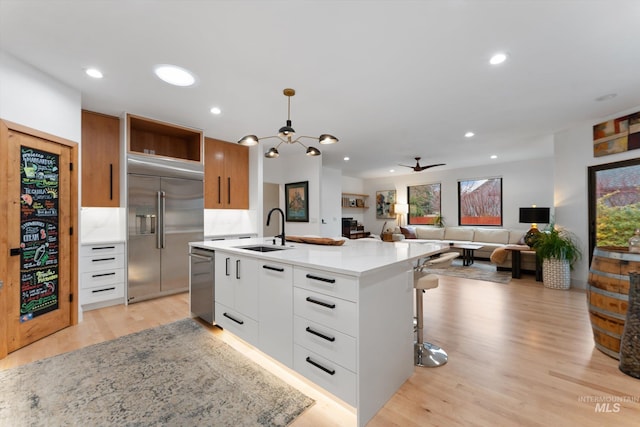 kitchen featuring sink, a center island with sink, pendant lighting, stainless steel appliances, and white cabinets