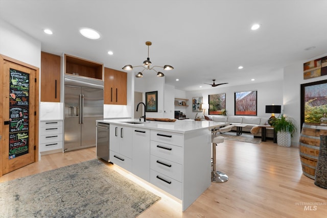 kitchen with pendant lighting, sink, white cabinetry, stainless steel appliances, and an island with sink