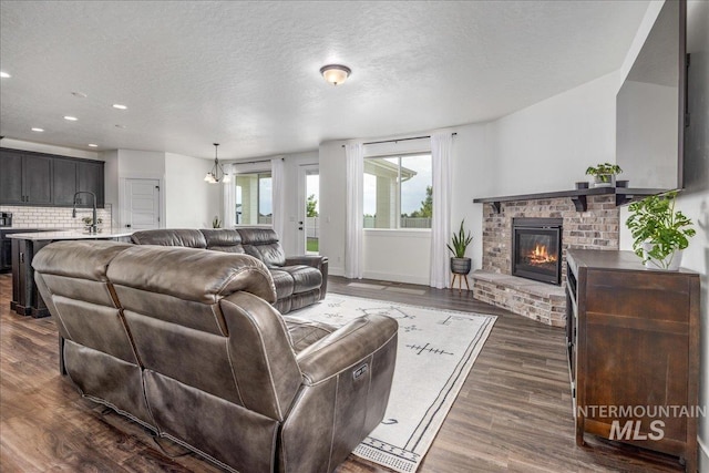 living area with dark wood-style floors, baseboards, recessed lighting, a textured ceiling, and a brick fireplace