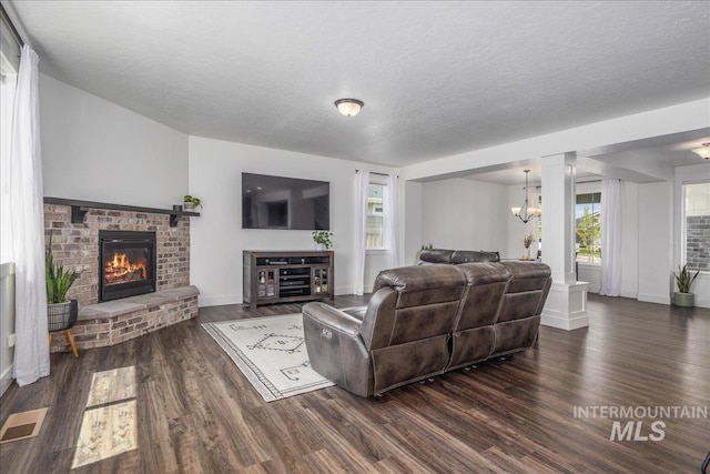 living room featuring visible vents, a textured ceiling, dark wood-style floors, an inviting chandelier, and a brick fireplace