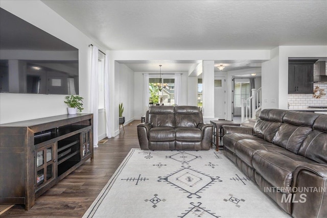 living area featuring baseboards, wood finished floors, a notable chandelier, a textured ceiling, and ornate columns