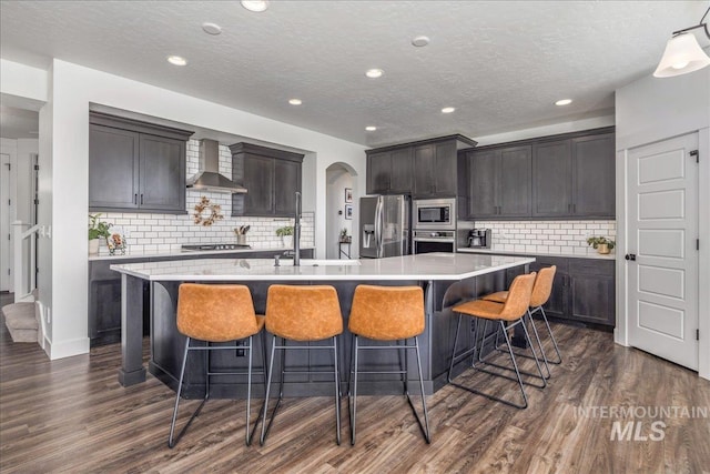 kitchen featuring stainless steel appliances, dark wood-type flooring, a large island, and wall chimney range hood