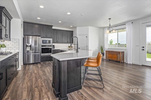 kitchen with light countertops, an island with sink, dark wood-style flooring, and stainless steel appliances