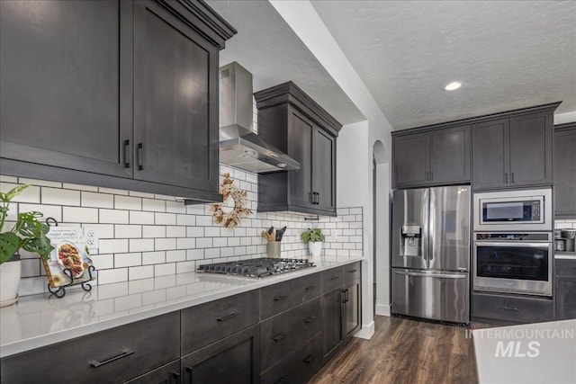 kitchen featuring dark wood-style floors, arched walkways, appliances with stainless steel finishes, a textured ceiling, and wall chimney range hood