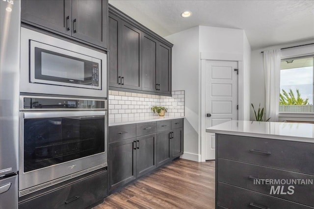 kitchen with recessed lighting, appliances with stainless steel finishes, light countertops, decorative backsplash, and dark wood-style flooring