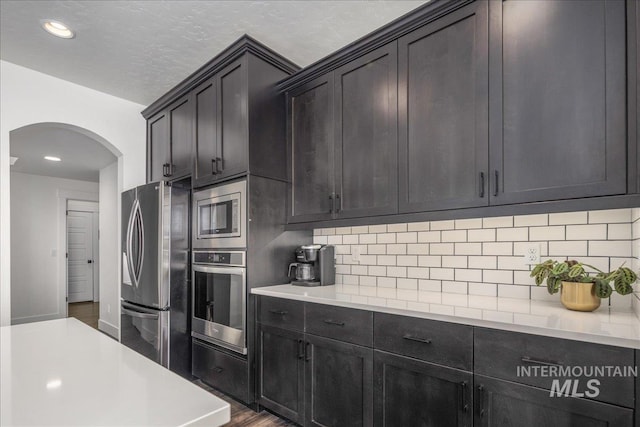 kitchen with arched walkways, backsplash, appliances with stainless steel finishes, and light countertops