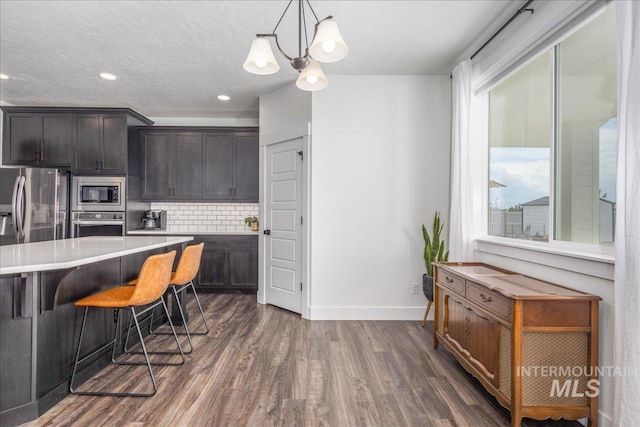 kitchen featuring a breakfast bar area, dark wood finished floors, stainless steel appliances, light countertops, and backsplash