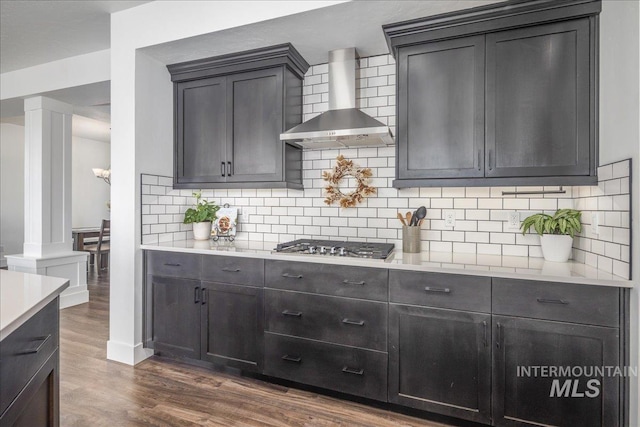 kitchen featuring light countertops, wall chimney exhaust hood, ornate columns, and dark wood-style flooring