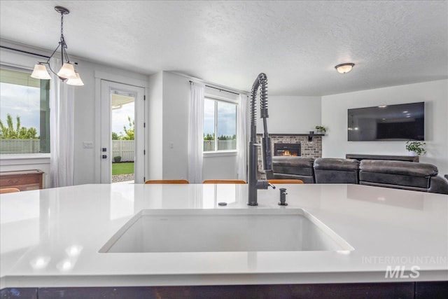 kitchen featuring a fireplace, a sink, a textured ceiling, decorative light fixtures, and open floor plan