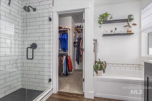 bathroom with a walk in closet, wood finished floors, a bath, and a shower stall