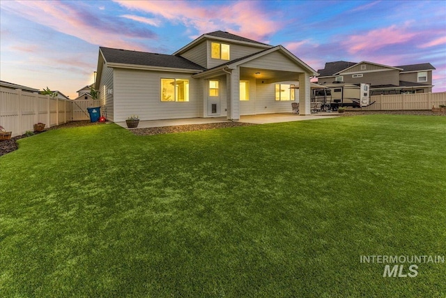 back of property at dusk with a fenced backyard, a yard, and a patio